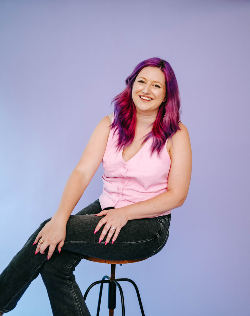 Photography Coach | Karinda K | Karinda smiling while sitting in a purple studio