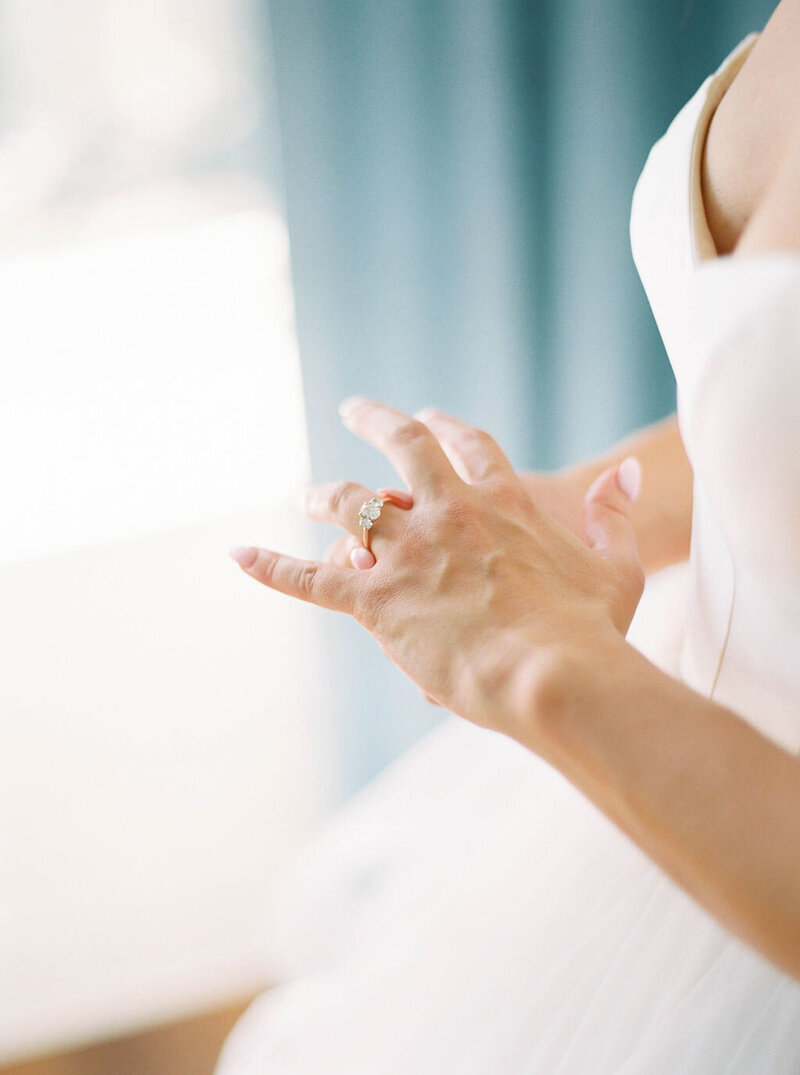 Wedding Photographer RI | Close-up of a bride's hands, gently placing a diamond ring on her finger. She wears a white gown. 