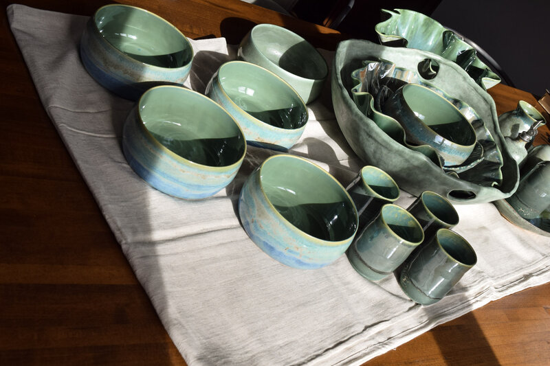 A table is set with a collection of green tableware including pasta bowls, drinking glasses, serving dishes and oil bottles