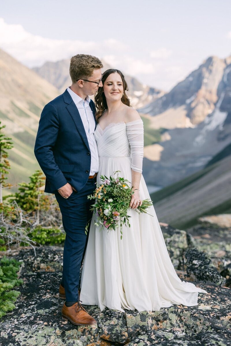 This heartfelt photograph captures a bride and groom holding each other after a scenic hike at Moraine Lake in Banff National Park. Surrounded by the iconic turquoise waters and dramatic mountain peaks, their embrace symbolizes their adventure and commitment in one of nature’s most stunning settings.