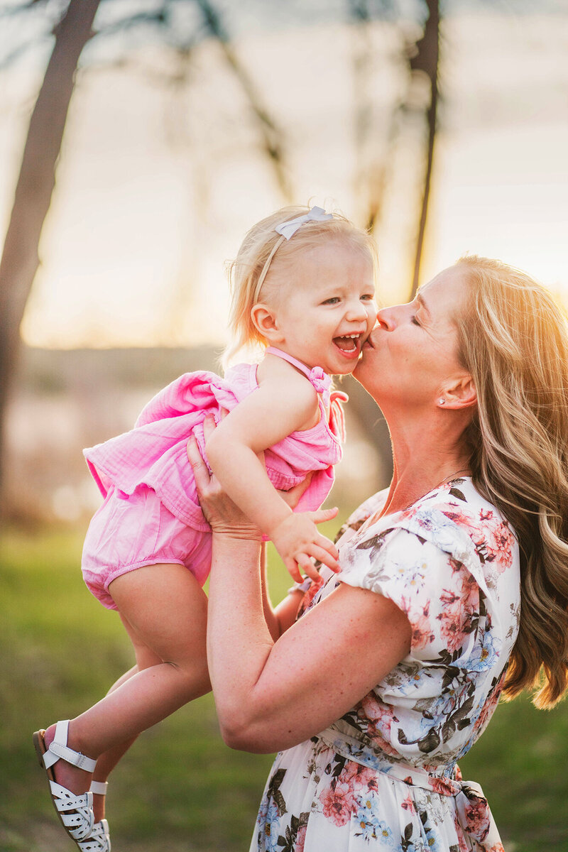 Mom and toddler girl swing around and laugh and smile brighting in golden light in Denver Colorado.