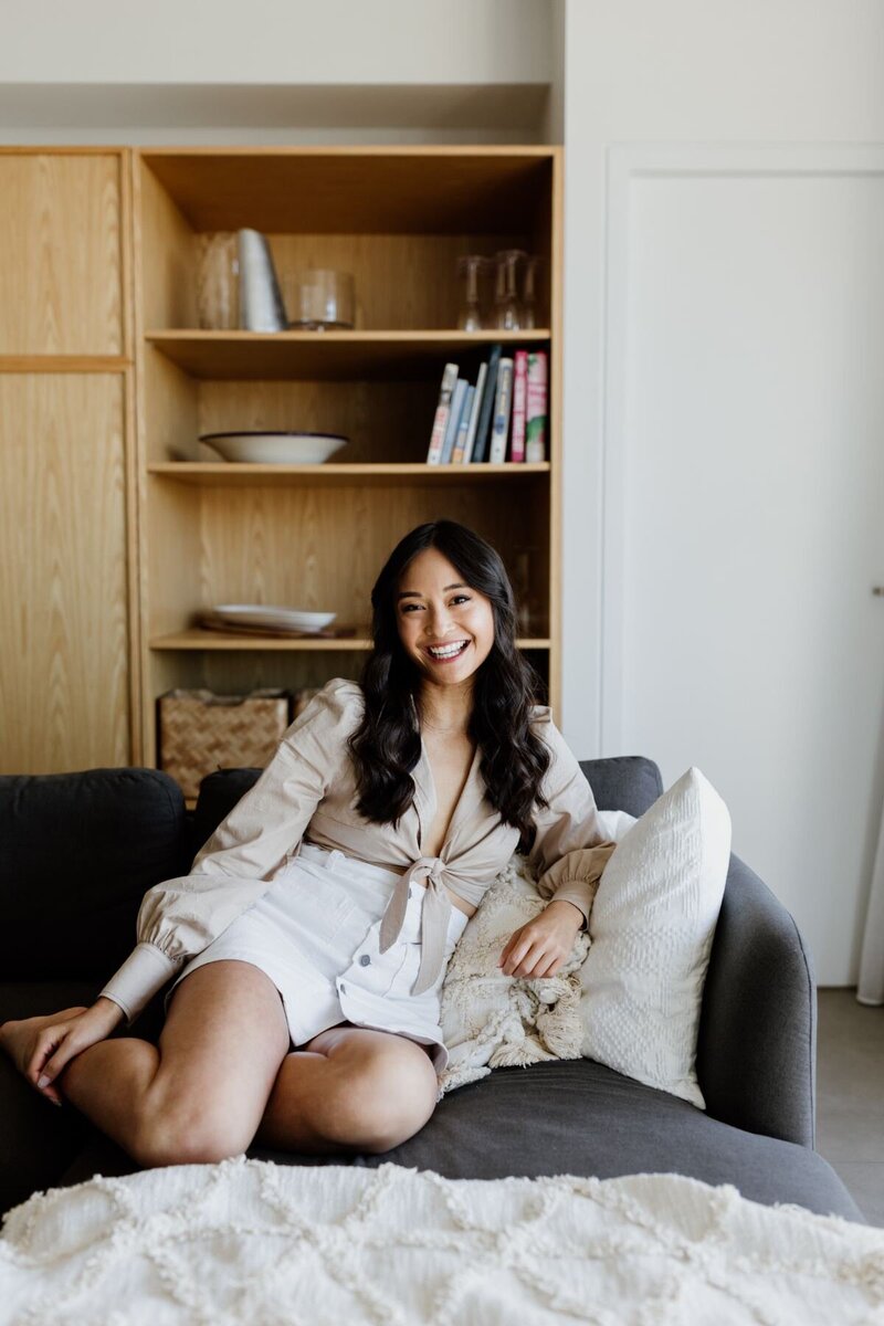 Trang Nova sitting on a couch warmly smiling at the camera.