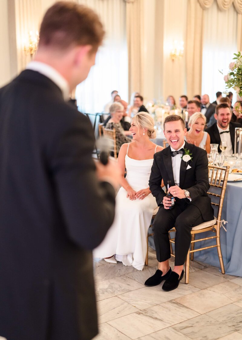 A bride and groom sit at the front of the head table inside the Westin Columbus and laugh during the speeches