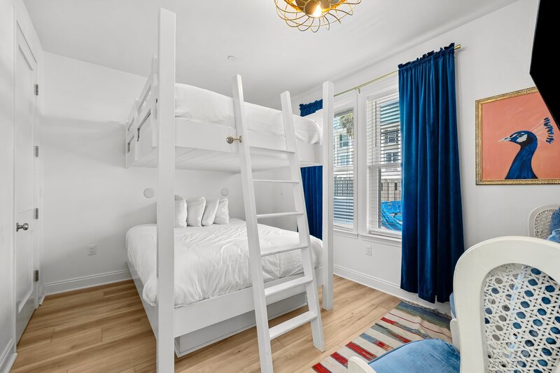 Coastal-chic downstairs bunk room with queen-over-queen bunks, bold blue curtains, and natural light—perfect for families and groups visiting PCB or 30A.