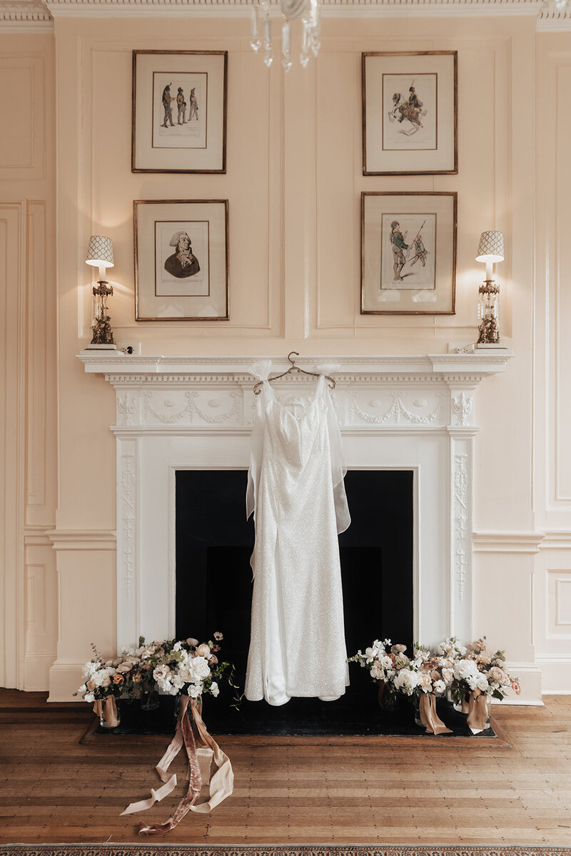 Weddings dress hanging at fireplace surrounded by flowers at lowndes grove