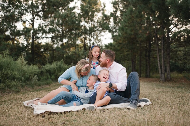 Family of five sitting on the ground laughing at each other by Cypress Family Photographer