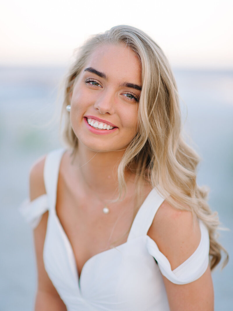 Beautiful close-up of smiling senior girl in white dress with soft beach background in Charleston, SC