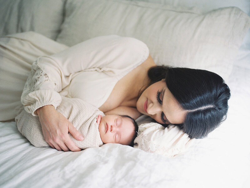 New mother laying on her bed cradling her newborn photographed by DC Newborn Photographer Marie Elizabeth Photography