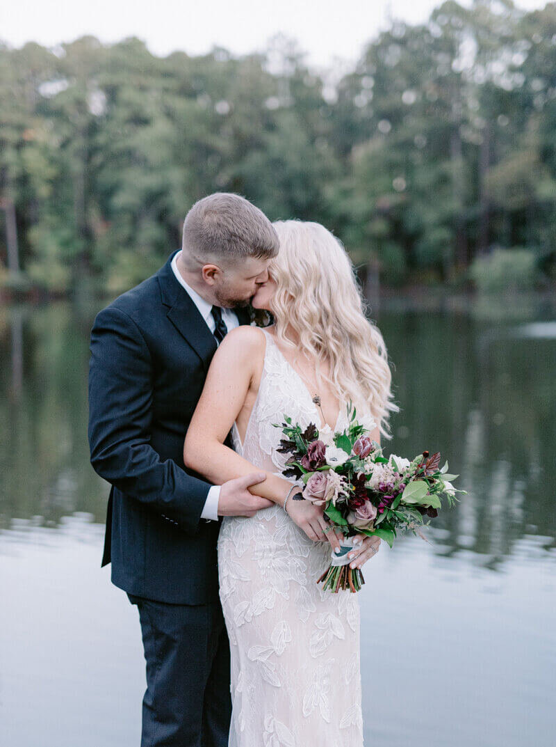 Married couple kissing on their wedding day in front of pond at Aldridge Gardens in Hoover, AL