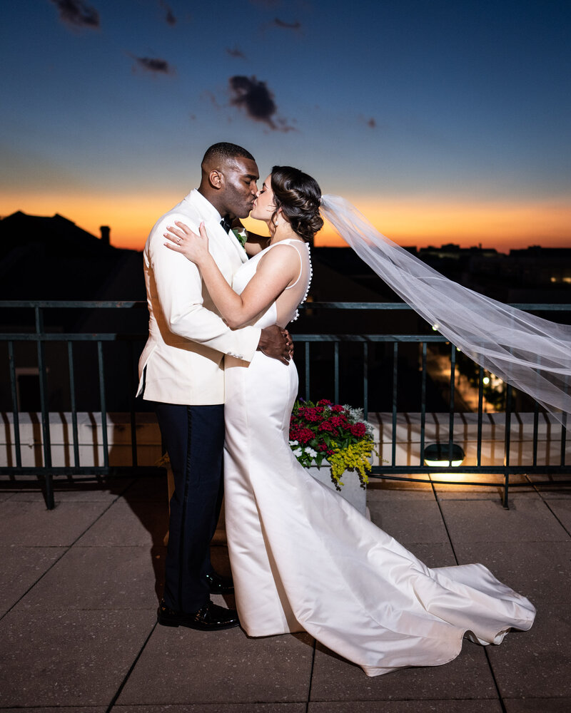 Bride and groom kiss at Riverview Room with sunset in background