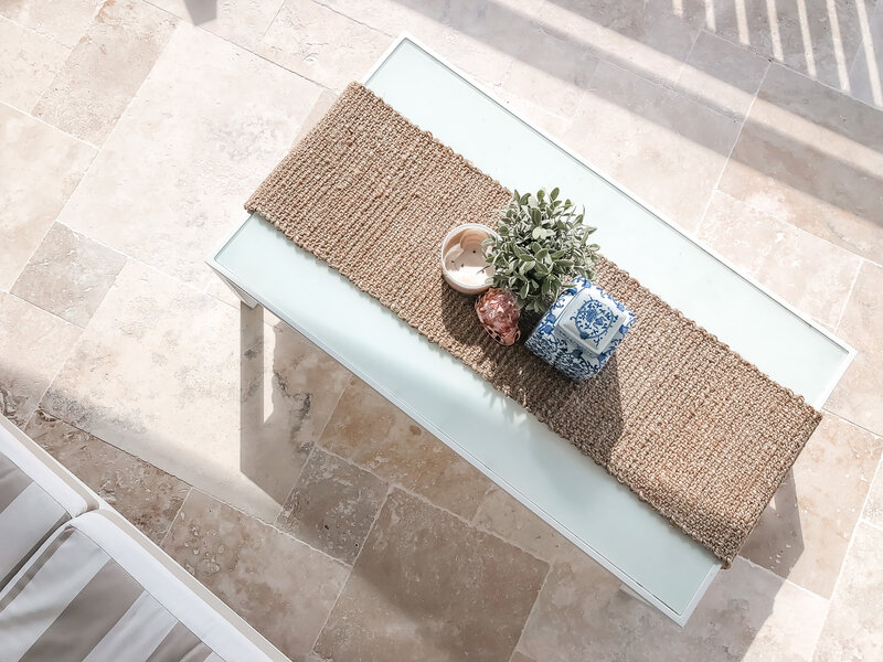 Top view of a table featuring a jute runner, small potted plant, candle, and blue-patterned jar on a tiled floor, showcasing the elegance brought by Custom Interior Design Newcastle.