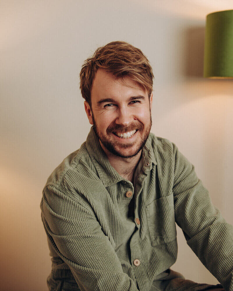 Tom Keenan smiling warmly while seated, wearing a green shirt.