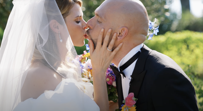 Close-up of bride and groom sharing a tender kiss in the garden after the ceremony, with vibrant florals and golden light — cinematic moment from a wedding video in Montenegro