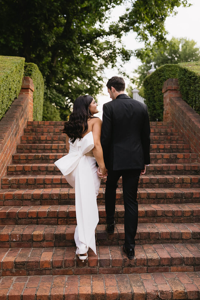 bride with bow on dress walking up stairs with husband