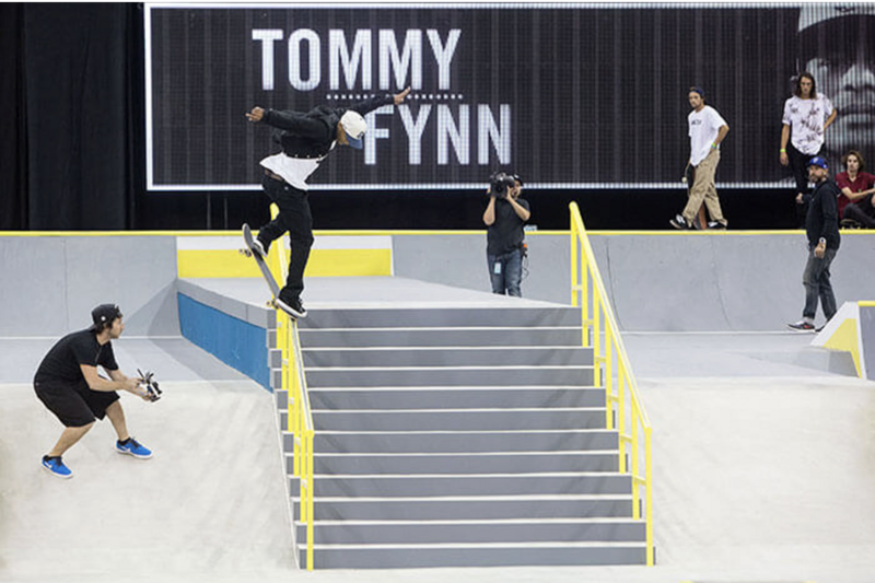 Tommy Fynn performing a trick on custom-built stairs and rail feature during a live skateboarding event