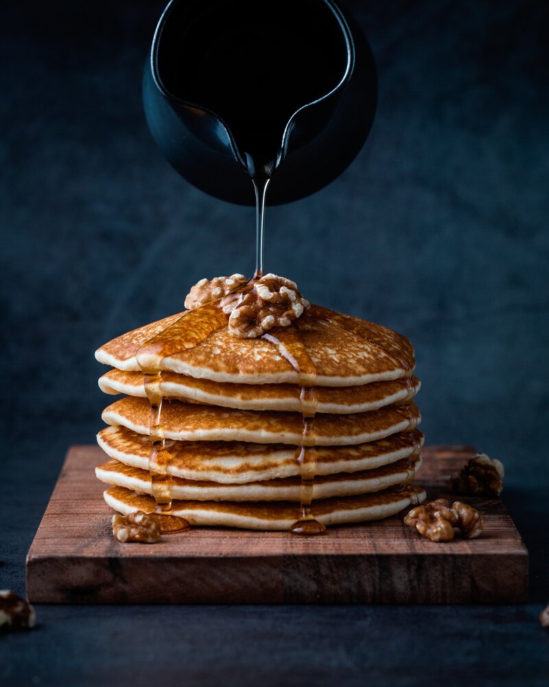 someone pouring syrup on a stack of pancakes