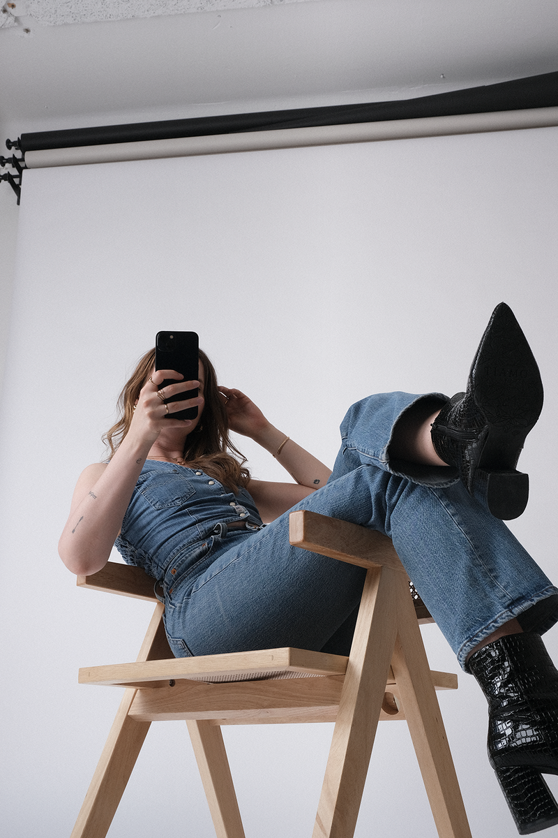 A woman sitting down on a chair and scrolling a mobile-friendly version of a website. She's wearing a blue jeans suit and black heels.