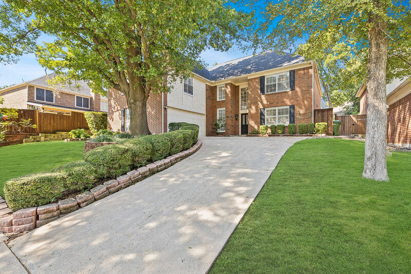 Stunning curb appeal at 502 Yaupon Drive with classic brick exterior, arched windows, mature trees, and lush landscaping on a spacious corner lot.