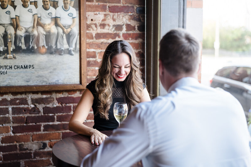 An engaged couple sit at a table by the window in German Village and laugh together