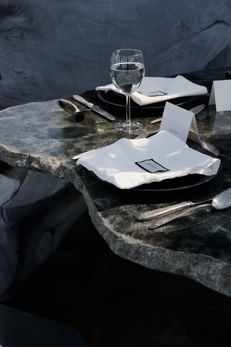 Sun shining on a table decked with plates, a glass of champagne and Gucci napkins
