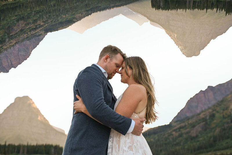 Sun sets over mountains in Glacier National Park while Bride and Groom embrace