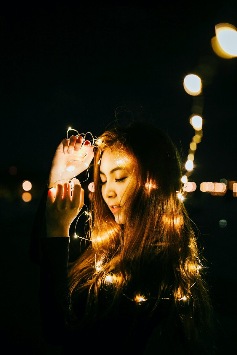 Young Asian Woman against a black background with fairy lights and bokeh effects