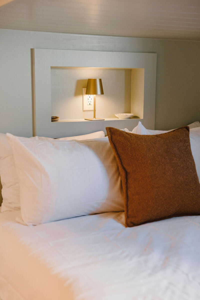 white bed linens, brown pillow, gold lamp
