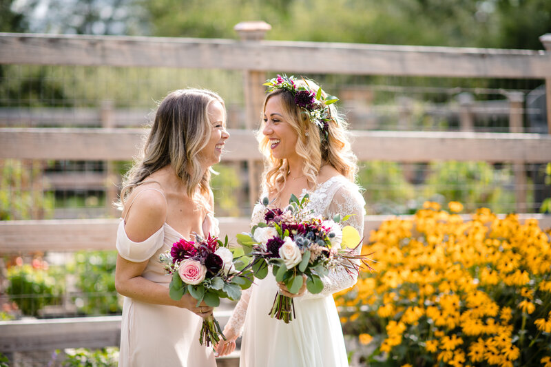 Bride and bridesmaid smile in a field of flowers outside at a  berkshires wedding venue