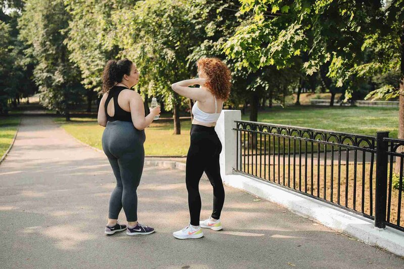 Two women wearing leggings pose in a park, highlighting an active lifestyle and sports nutrition support in Chicago.