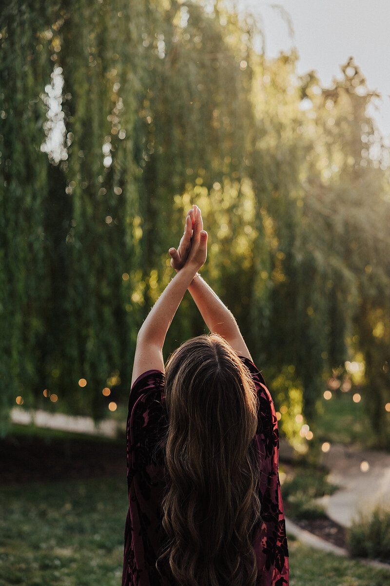 a woman with her hands out stretched to the sky in front of trees 