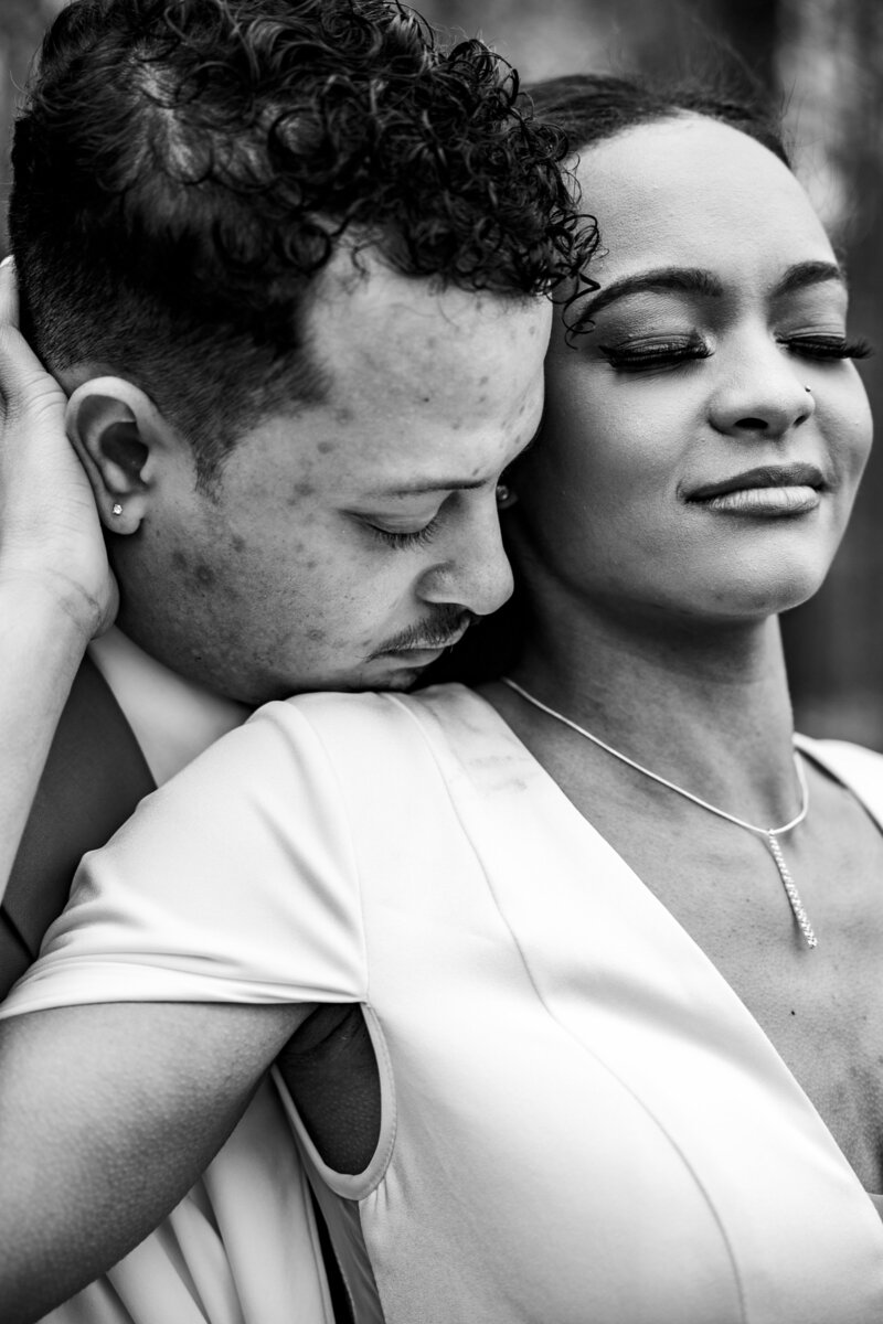 Close-up of a woman's engagement ring as she holds an umbrella, her fiancé gently holding her face in a romantic moment.