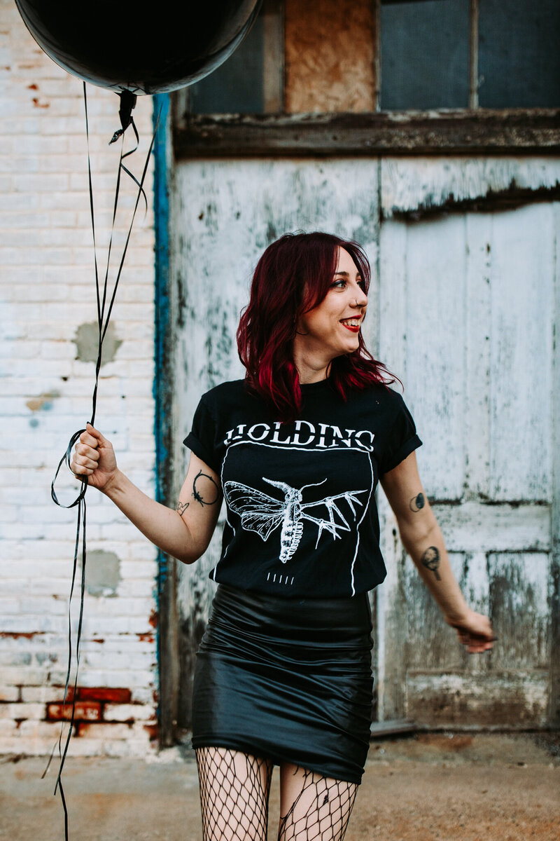 A wedding photographer with balloons in her hand and a goth aesthetic with a band tee