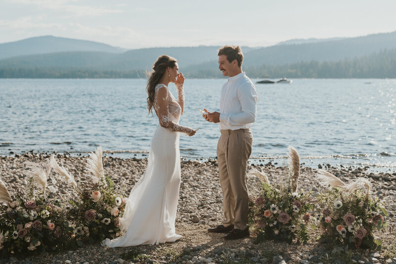 Bride wiping away a tear while groom reads his vows in front of lake by Big Sur Elopement Photographer Kasey Mantiply