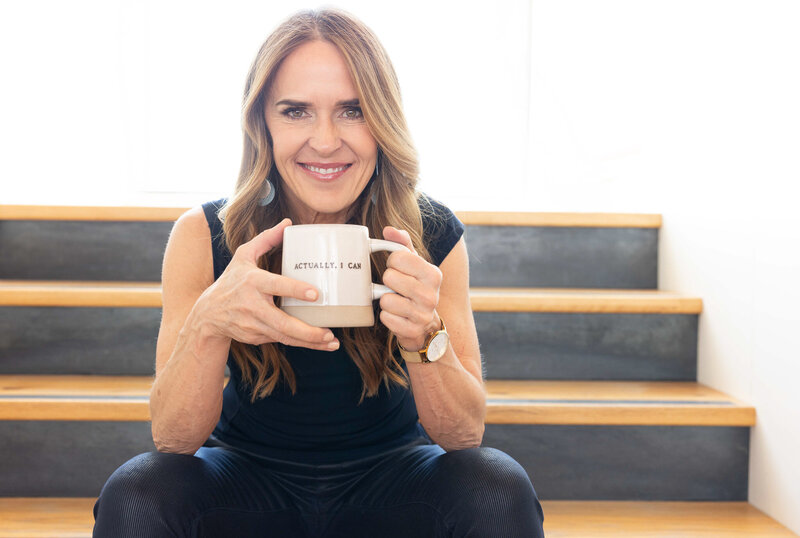 Fitness instructor sitting on wooden steps holding coffee mug