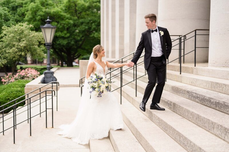 A groom in a black tux leads his bride up the stairs of the Ohio Statehouse