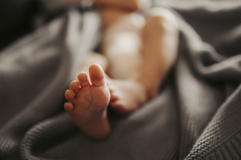 Lifestyle newborn photographer in Tifton, GA: image focuses on newborn baby's foot, with the rest of the baby out of focus, lying in a blue blanket