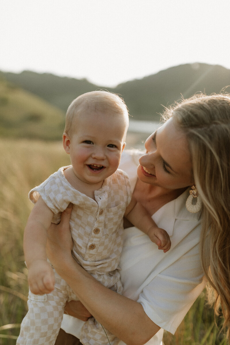 Kaity from Rainstorm Photo & Video holding her baby and smiling in golden light, captured with warmth and authenticity among the Indiana dunes.