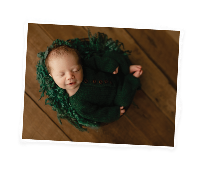 newborn posed in a bowl in green on a wooden floor.
