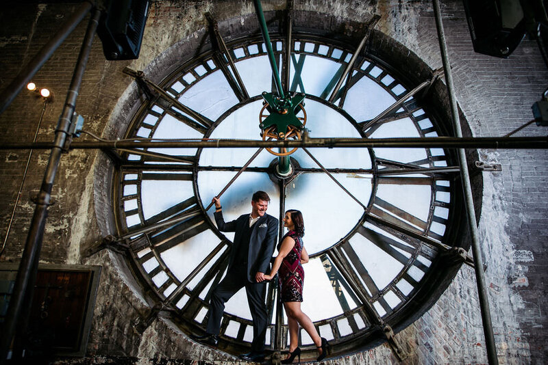 A couple holding hands and smiling at each other inside the clock face of the bromo seltzer tower.