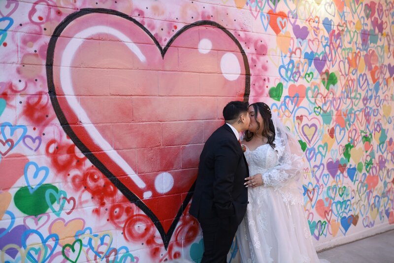 Bride and groom kiss in front of a colorful heart mural on their wedding day in Indianapolis