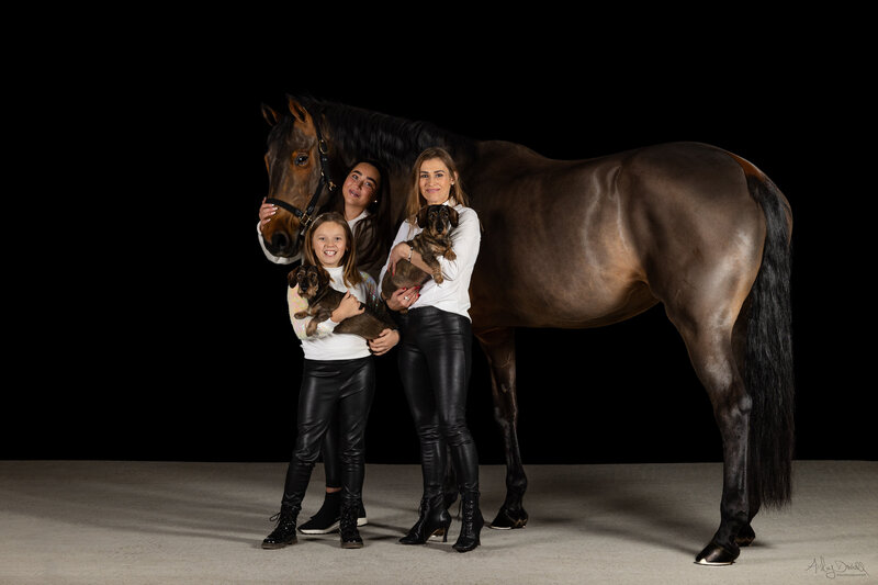 family portrait on black background with mother daughters dogs and a horse