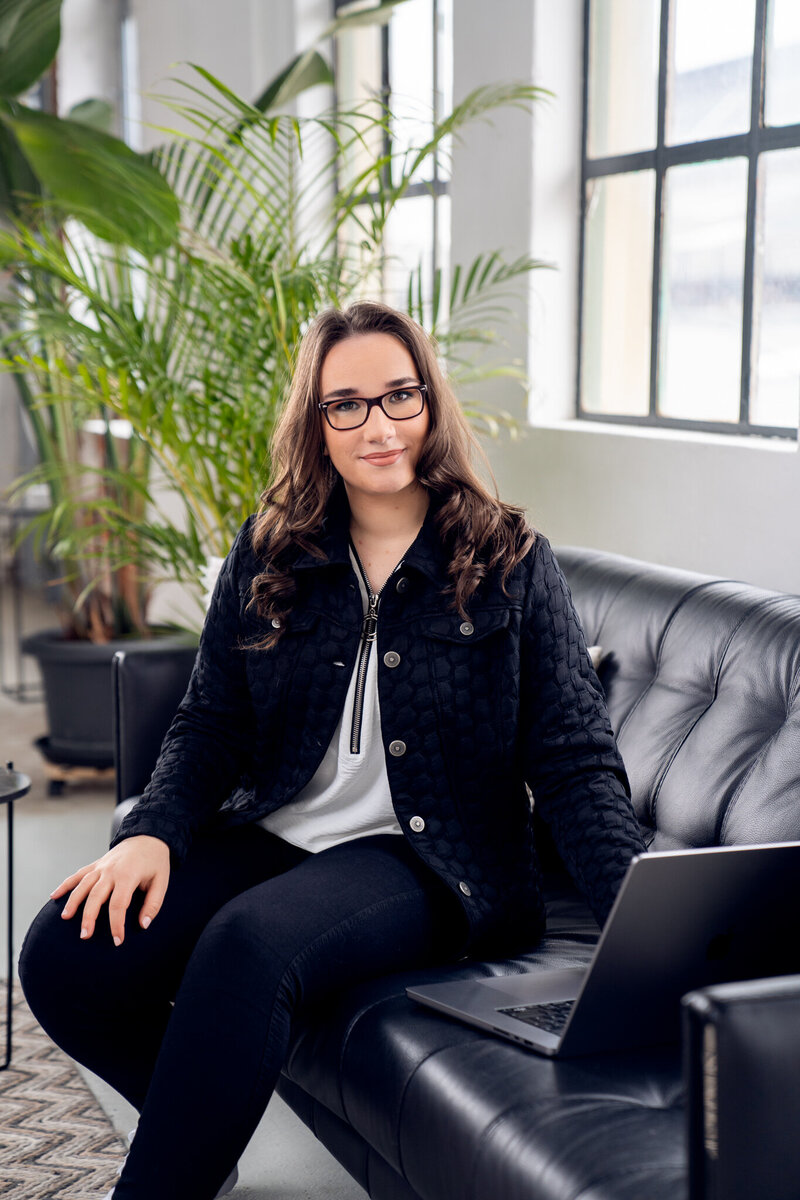 Franziska Pirro sitting with her MacBook on a couch, looking into the camera with a plant in the background