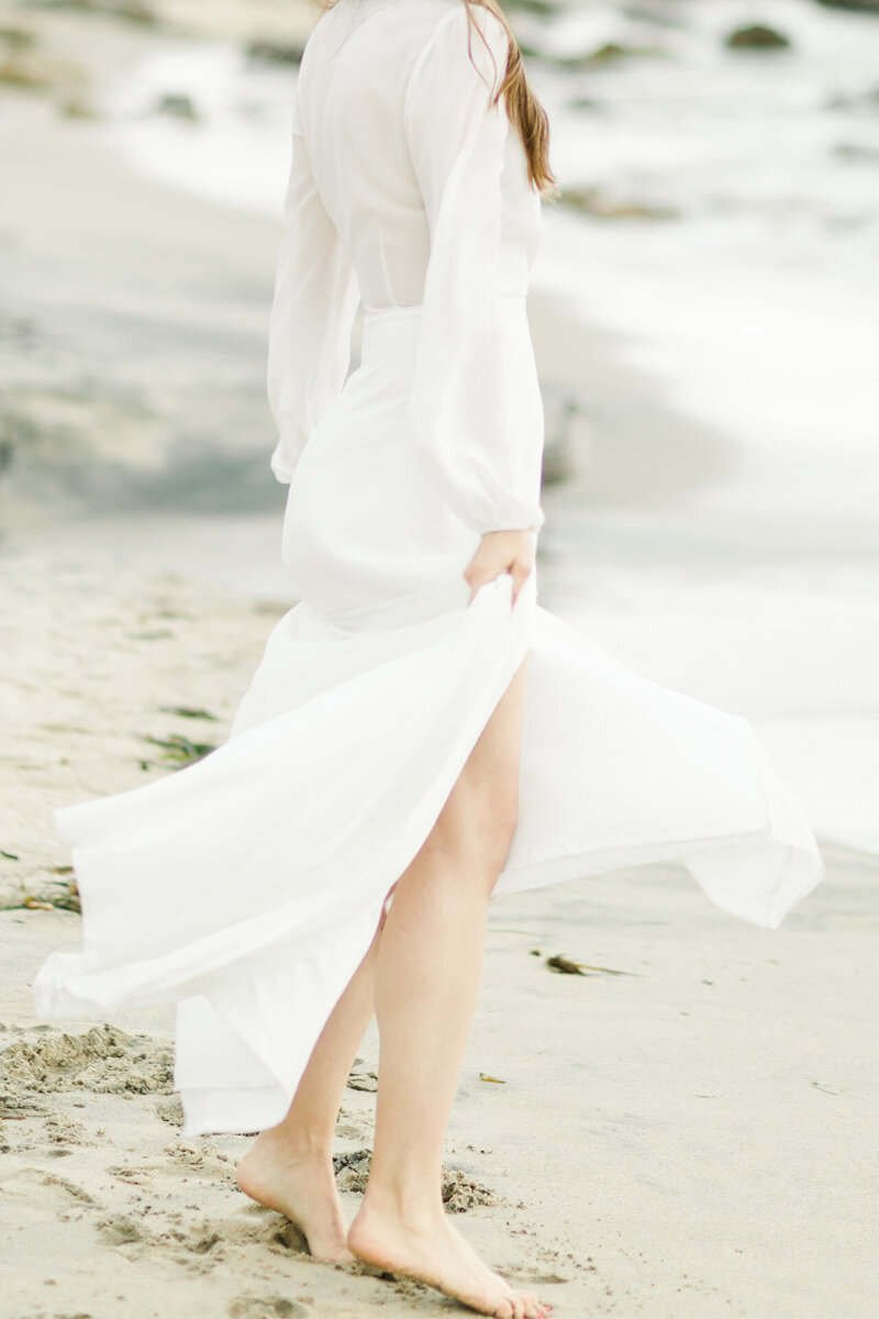 Woman in white gown walks down the beach