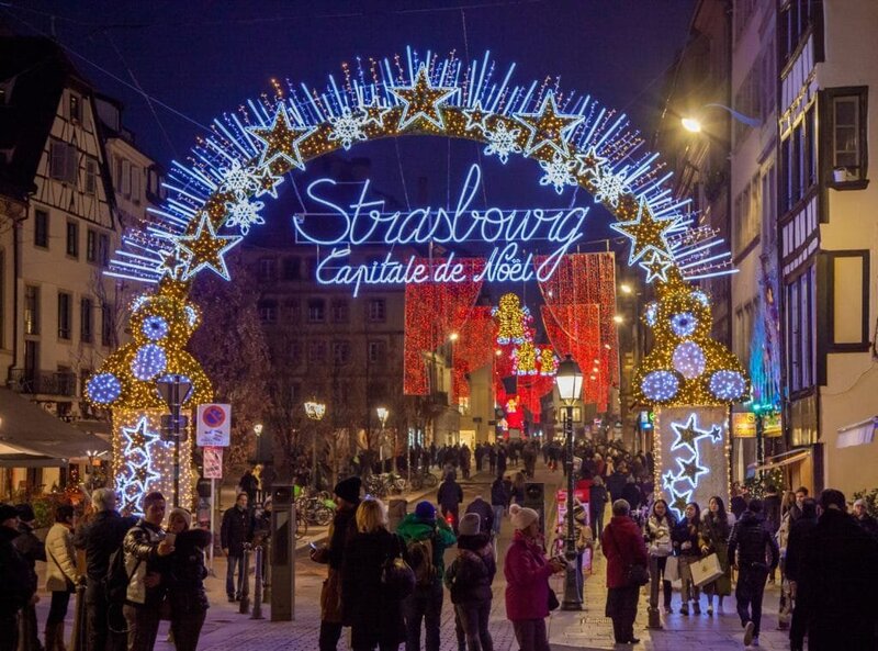 Holiday decorations and lights across the buildings with the Strasbourg Capitale de Noel sign light up for the night time Christmas markets