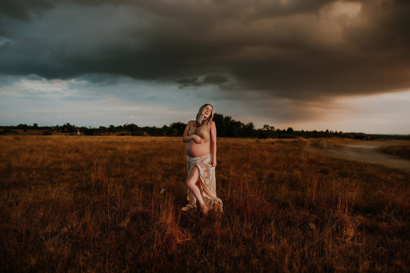 Expecting mom in a vintage set standing in a field during a moody sunset.