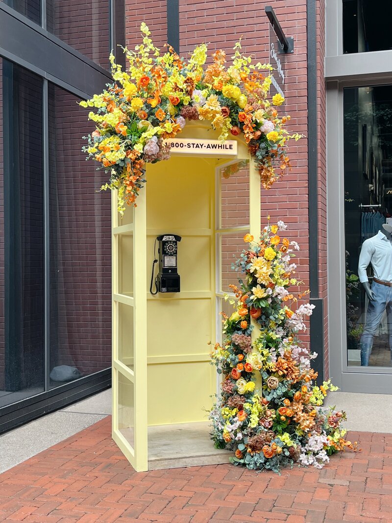 Spring phone booth, photo moment, floral installation. Retail shopping floral installation with bright yellow, orange, pink colors and silk florals. Design by Rosemary and Finch in Nashville, TN.