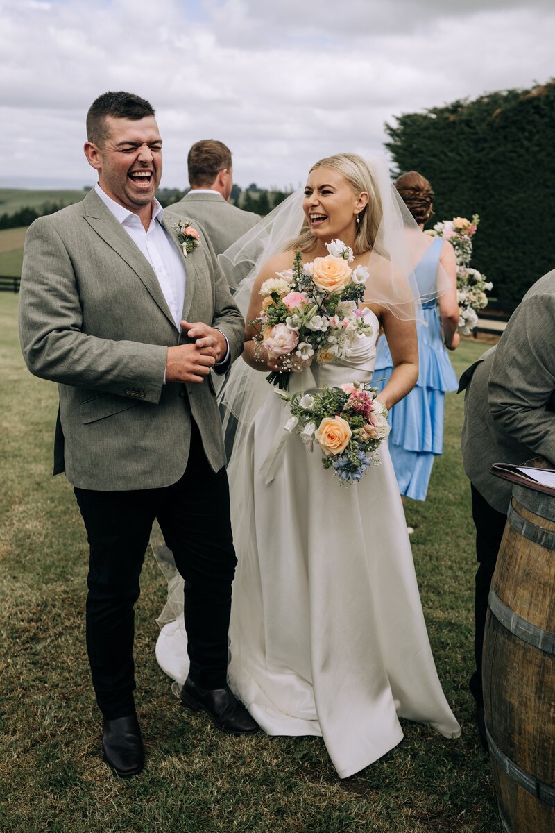 bride and groom laugh on the lawn at their wedding at the farm chapel waimumu