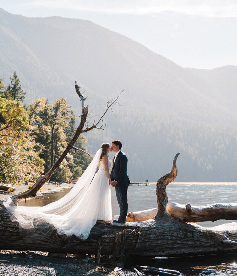 A couple stands and kisses on a log at Lake Crescent in Olympic National Park after their elopement