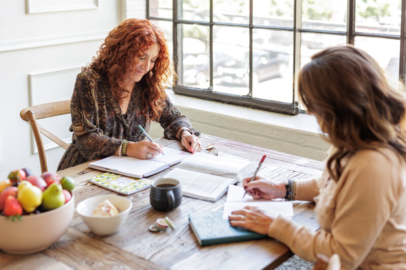 Two women sitting at table writing during a bible study lifestyle image during product based business team branding photoshoot session