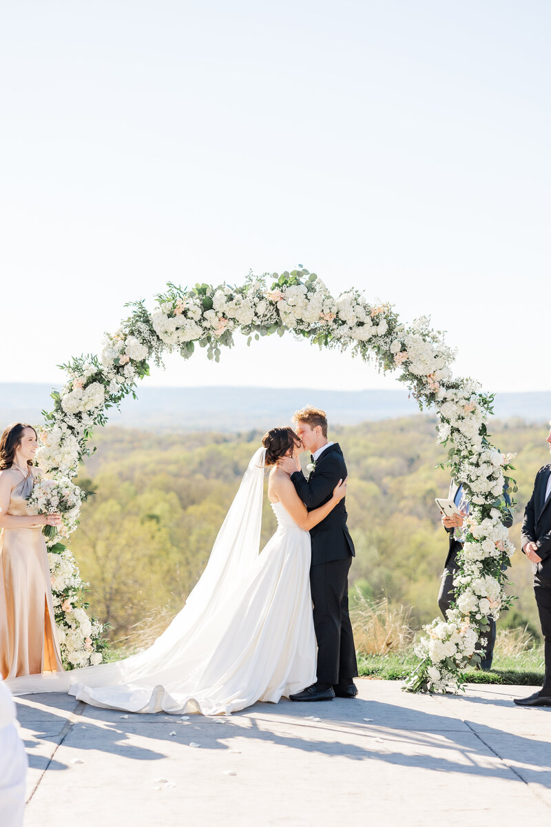 a bride and groom kissing under a floral arch